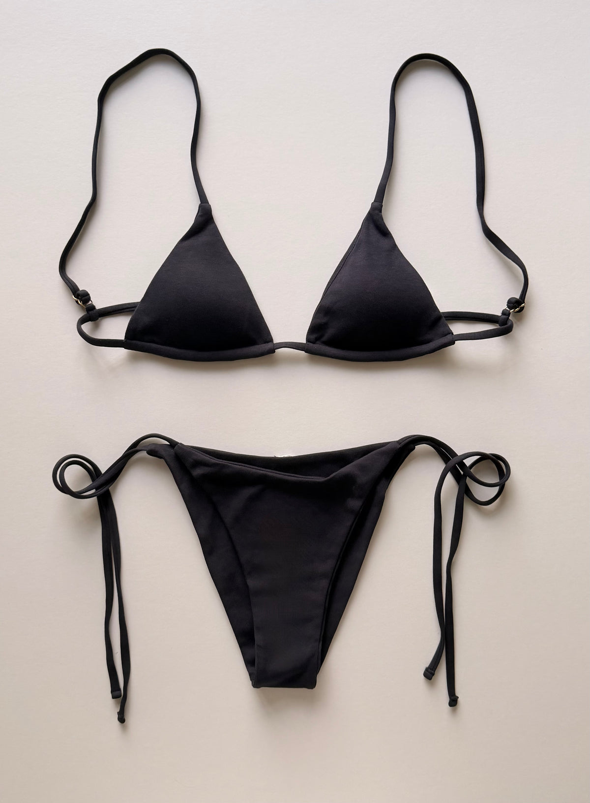 A two-piece dark navy string bikini set laid flat on a light beige background, featuring a triangle top with adjustable side straps and matching side-tie bikini bottoms.